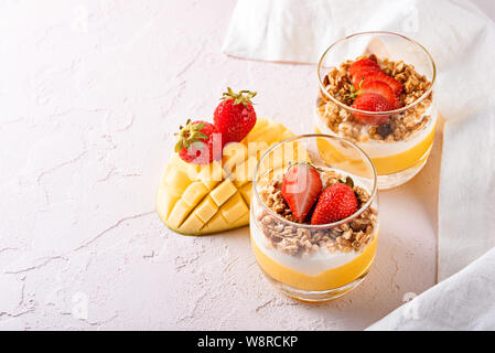 Vista dall'alto di due bicchieri con dessert di frutta del frullato di mango, ricotta, granola e fragola con splendidi fette di mango e copia spazio su p Foto Stock