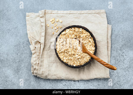 Fiocchi d'avena o fiocchi di avena in ciotola di legno su lino tessile, vista dall'alto. Cibo sano, dieta e pulire il concetto di mangiare Foto Stock