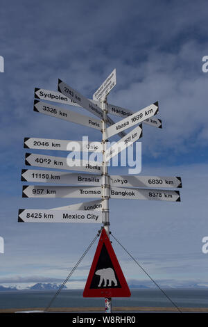 Una indicazione di distanze di world-wide città e paesi dalle Svalbard aeroporto, Longyearbyen con un orso polare in segno di avvertimento di seguito. Foto Stock