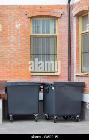 Due nero nel cestino dei rifiuti i contenitori sotto le finestre di un edificio in mattoni. I contenitori in plastica per la raccolta di rifiuti separati, lo smistamento dei rifiuti, dell'inquinamento. Wa Foto Stock
