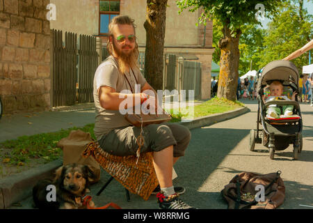 Cesis, Lettonia - 19 Luglio 2019: un musicista di strada con un cane in una giornata di sole Foto Stock