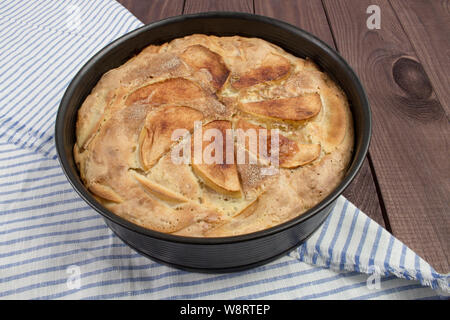 La torta di mele in casa in una teglia su una tavola di legno con una a strisce blu igienico. Torta di mele, fette di mele sono sulla superficie, paste dolci Foto Stock