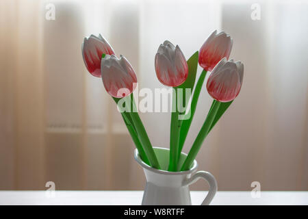 Bouquet di rosso e bianco di tulipani di legno in una caraffa del bianco contro la finestra e delicato tulle Foto Stock