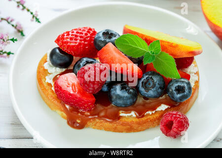 Una deliziosa prima colazione. Delicatezza Toast sandwich con crema di formaggio o di mascarpone, caramello (iris toffee) e frutti di bosco freschi - mirtilli, lamponi, str Foto Stock