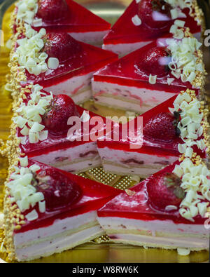 La torta di fragole con strati di SOUFFLE e biscuit, confettura di fragole con frutti di bosco e scaglie di cioccolato, cosparso con noci tritate. Pezzi triangolari di Foto Stock