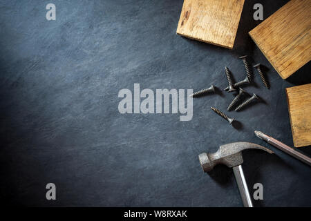 Il martello e il legname nero su sfondo di cemento. Vista superiore e copia spazio per il testo. Concetto di falegname o costrutto. Foto Stock