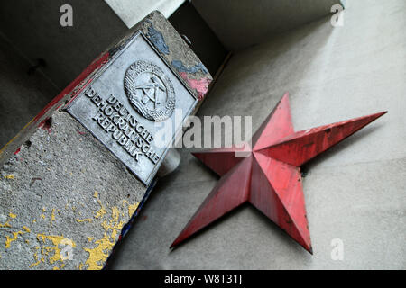 Il dettaglio di una pietra di confine a Berlino con il logo della Repubblica democratica tedesca e una rossa Stella sovietica sulla facciata della casa. Foto Stock