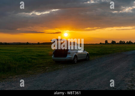 Una macchina parcheggiata su un campo al tramonto in un paesaggio rurale in Guelpe, Brandeburgo, Germania Foto Stock