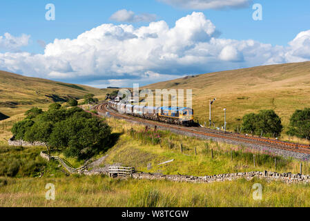 Una classe 66 loco traina un carico del treno di pietra proveniente dalla cava di Arcow fuori della rotaia sciavero a Blea Moor sul Settle-Carlisle linea ferroviaria. Foto Stock