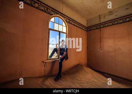 Tourist si trova nella finestra di una camera nella città fantasma Kolmanskop, Namibia Foto Stock