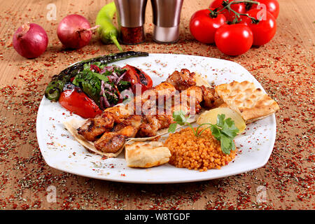 Spiedini di pollo che serve di pollo con sugo di carne e verdure fresche sulla piastra bianca sulla tabella riempita con spezie piccanti Foto Stock
