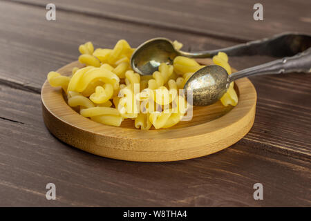 Sacco di tutta la pasta grezza gemelli sulla piastra di bambù con pinze da zucchero su legno marrone Foto Stock