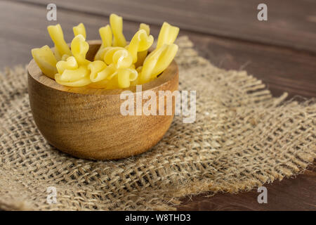 Sacco di tutta la pasta grezza gemelli nella ciotola di legno sulla stoffa di iuta su legno marrone Foto Stock