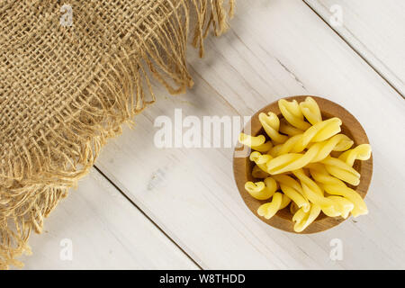 Sacco di tutta la pasta grezza gemelli nella ciotola di legno con stoffa di iuta flatlay su legno bianco Foto Stock