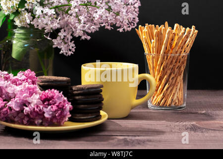 Tea party, giallo cup, biscotti con scaglie di cioccolato e bastoni dolce decorato con fiori di Syringa. Impostazione tabella dolce con posizione orizzontale Foto Stock