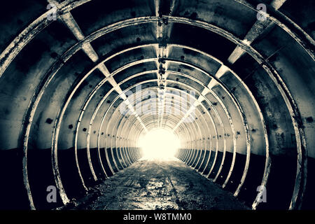 Astrazione per lo sfondo. Galleria anulare con costole rigide e luminose alla fine. cemento costruzione militare. In bianco e nero. Oscurata. Foto Stock