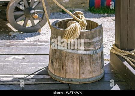 Cucchiaio di legno con una corda si erge sul coperchio di un pozzo nel cortile del castello medievale nella città estone di Rakvere. Foto Stock