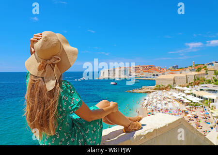 Bella giovane donna con cappello seduti sulla parete guardando stupenda vista panoramica dal villaggio di Dubrovnik in Croazia, Europa Foto Stock