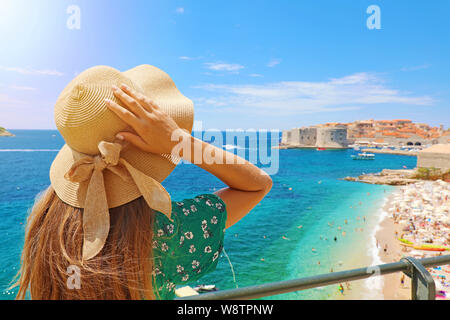 Vacanze estive in Croazia. Vista posteriore della giovane donna che mantiene il suo cappello con Dubrovnik Città sullo sfondo, Croazia, Europa. Foto Stock