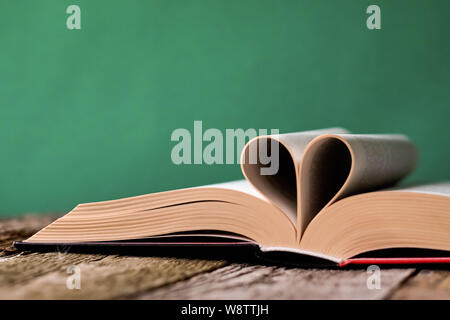 Si torna a scuola concetto, libro aperto e le pagine ripiegate a forma di cuore su un vecchio superficie di legno su uno sfondo di colore verde pulito chalk board, selectiv Foto Stock
