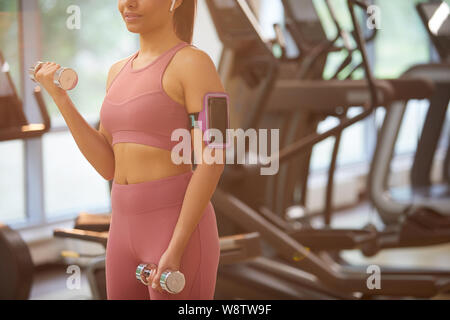 La sezione centrale Ritratto di giovane donna che lavora fuori nella palestra del peso di sollevamento con focus su smartphone nel supporto del braccio, spazio di copia Foto Stock