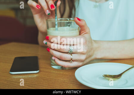 Vetro trasparente con caffè in mano di una ragazza con lo smartphone giacente sul piano portapaziente Foto Stock