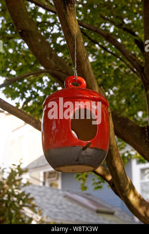 Rosso e nero ceramica bird feeder o birdhouse appeso a un albero in un giardino Foto Stock