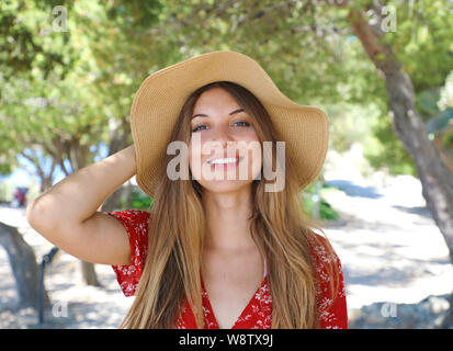 Ritratto di una bella ragazza sorridente indossando un cappello e vestito rosso guardando la fotocamera all'aperto Foto Stock