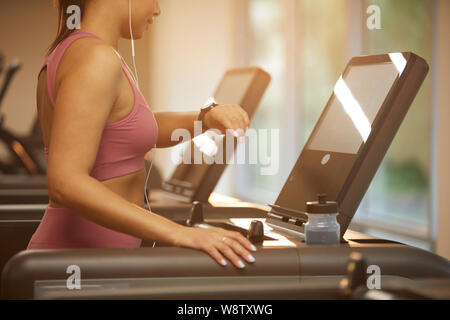 La sezione centrale Ritratto di giovane e bella donna in corsa sul tapis roulant in palestra e controllo smartwatch durante l'allenamento cardio, spazio di copia Foto Stock