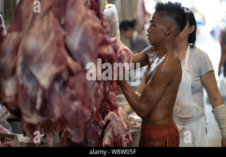 Un giovane ragazzo gestisce appendere le carcasse di carne entro il mercato del carbonio,Cebu City, Filippine Foto Stock