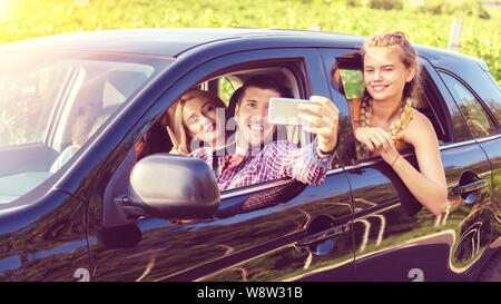 Felice giovani amici prendendo selfie mentre viaggiano insieme in auto Foto Stock