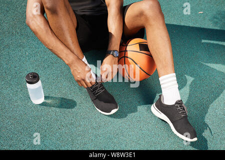 Sezione bassa ritratto di contemporaneo afro-legatura uomo calzature sportive nel campo da basket all'aperto, copia di sfondo spazio Foto Stock