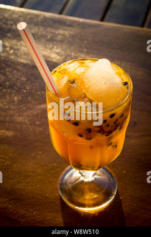 Fresco tropicale di granadiglie succo con ghiaccio e una cannuccia di plastica in un vetro su una tavola in legno rustico Foto Stock