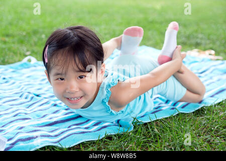 Poco toddler girl posa su asciugamano nell'erba su un giorno di estate Foto Stock