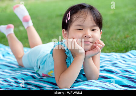 Poco toddler girl posa su asciugamano nell'erba su un giorno di estate Foto Stock