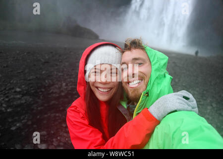 Selfie giovane prendendo immagini dello smartphone di cascata all'aperto di fronte Skogafoss in Islanda. Paio di visitare famose attrazioni turistiche e punti di interesse in natura Islandese in orizzontale sul Ring Road. Foto Stock