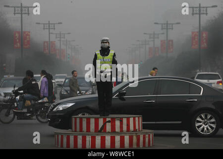 --FILE--un semaforo con un funzionario di polizia che indossa una maschera facciale dirige le auto su una strada di smog pesante nella citta' di Xian, porcellane del nord della provincia di Shaanxi, 2 febbraio 2014 Foto Stock