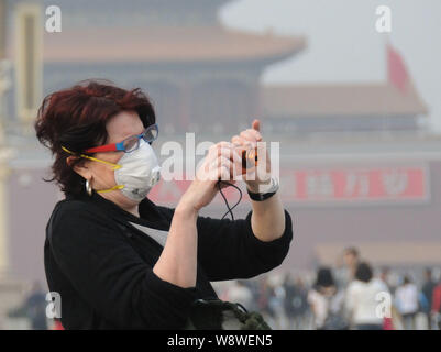 Un turista straniero che indossa una maschera facciale prende le foto in piazza Tiananmen in smog a Pechino in Cina, 25 marzo 2014. Porcellane autorità meteorologica Foto Stock