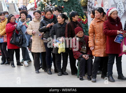 Una donna anziana si siede su una sedia come altri clienti stand in linea per lo scambio di mele per oro davanti ad un negozio di Gioielleria in Zhengzhou city, Centrale C Foto Stock