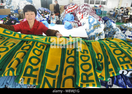 Una femmina di lavoratore cinese esamina le sciarpe di ventola del Brasile e la maglia della nazionale australiana per partite (Australia associazione nazionale squadra di calcio) prodotta per il 2014 Brasile Mondo Foto Stock