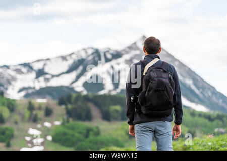 Uomo in piedi indietro closeup sul sentiero Snodgrass con sfondo bokeh vista del monte Crested Butte, picco di Colorado e il villaggio in estate Foto Stock