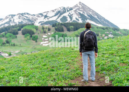 Uomo in piedi indietro sul sentiero Snodgrass con sfondo bokeh vista del monte Crested Butte, picco di Colorado e il villaggio in estate Foto Stock