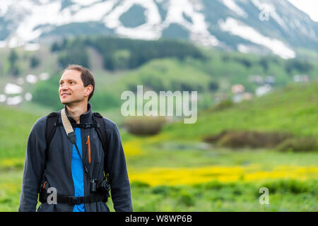 Uomo in piedi felici sul sentiero Snodgrass con fotocamera e sfondo bokeh vista del monte Crested Butte, Colorado e fiori di colore giallo Foto Stock