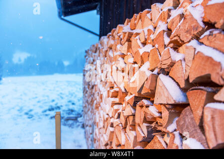 Full-sized vista laterale di appena battuto, impilati su un fienile e coperti di neve di legna da ardere in nevicata. Foto Stock