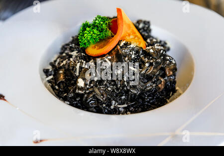 Squid ink risotto nero con anelli di totano cosparso con parmigiano, servita con una fetta di arancia e il prezzemolo in un ristorante di altissimo livello in Montenegro Foto Stock