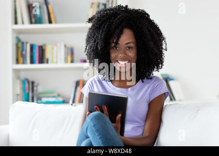 Ridendo americano africano Donna con computer tavoletta al chiuso in casa Foto Stock