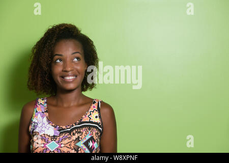 Bella americano africano donna che guarda lateralmente ad una parete verde Foto Stock