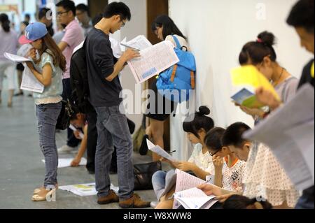 --FILE--laureati cinesi stand o squat come essi guardare le informazioni di lavoro a una fiera del lavoro in Hangzhou, est Chinas nella provincia di Zhejiang, 7 giugno 2014. Foto Stock