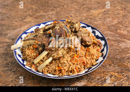 Riso pilaf con costolette d'agnello , in un piatto tradizionale con ornamenti , su un marrone textured background . Foto Stock