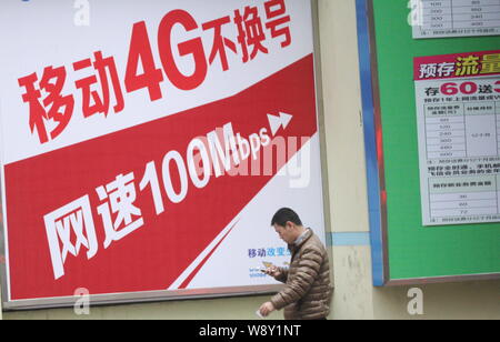 --FILE--un uomo cinese usa il suo smartphone come egli cammina davanti a un annuncio per il 4G servizi di China Mobile a Qingdao City East Chinas Shandong Foto Stock